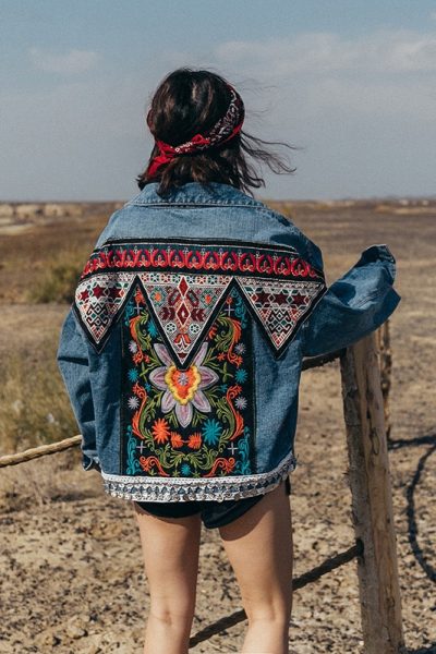 Veste en jean brodée style bohème à fleurs porté par une femme au bandana rouge devant un desert