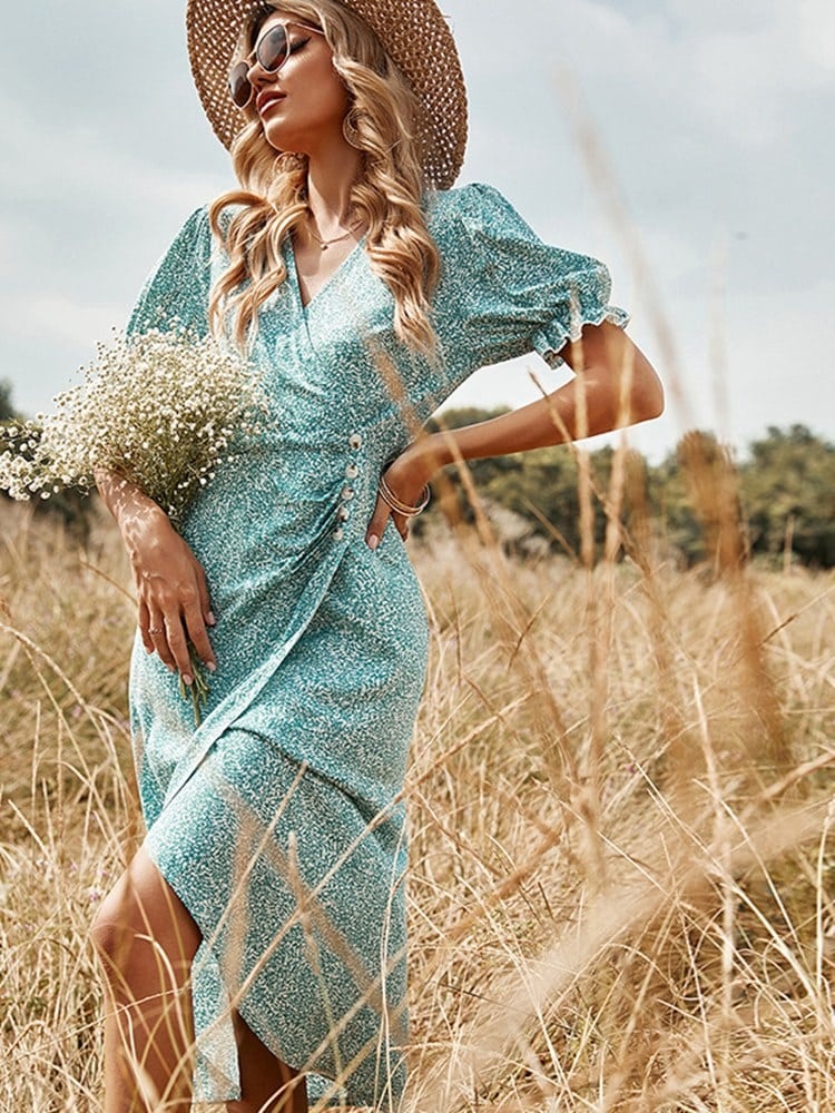 Femme portant une robe bleu à imprimé floral avec un bouquet dans sa main droite et un chapeau sur la tête le tout dans un champs