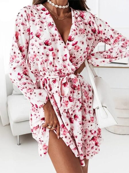 Femme portant une robe courte blanche avec un imprimé floral rose et un col en V la pièce autour d'elle est blanche et des meubles derrière elle
