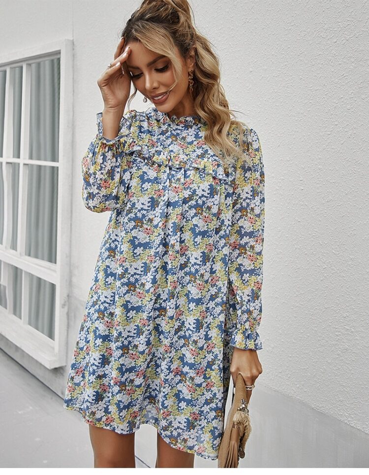 Femme portant une robe bleue avec des fleurs dans les tons jaune, blanc et rose et elle porte aussi une pochette dans sa main droite