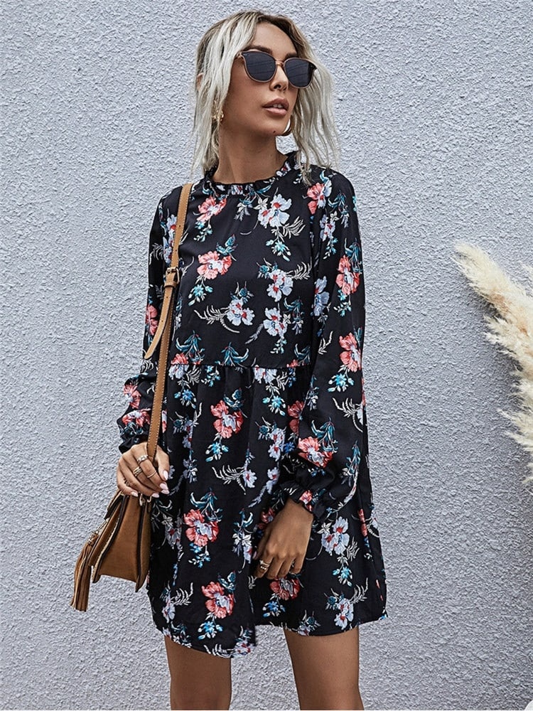 Femme portant une robe noir avec des fleurs colorés ainsi que des lunettes et un sac sur son épaule droit