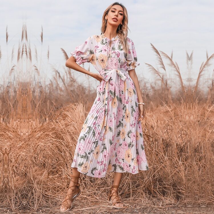 Femme blonde dans un champ de blé portant une robe longue plissée rose fleurie