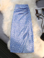 Jupe fleurie bleue étalée sur un tapis effet peau de bête en blanc avec un sac à main à droite posé sur un magazine