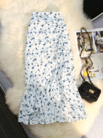 Jupe blanche avec des fleurs bleues étalée sur une peau de bête de type fausse fourrure blanche avec un sac noir à bandoulière à droite et un magazine ouvert