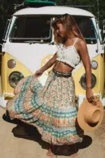 Femme se trouvant devant une camionnette blanche et jaune avec un crop top blanc laissant apparaitre son nombril et une jupe de style bohème qu'elle fait virevolter