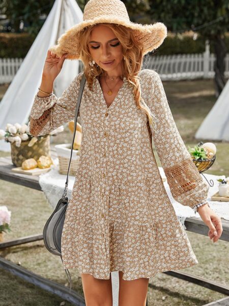 Femme blonde dans un jardin avec une table de pique-nique derrière elle. Elle porte une robe fleurie dans les tons beiges avec un chapeau en osier ainsi qu'un sac à main sur son épaule droite