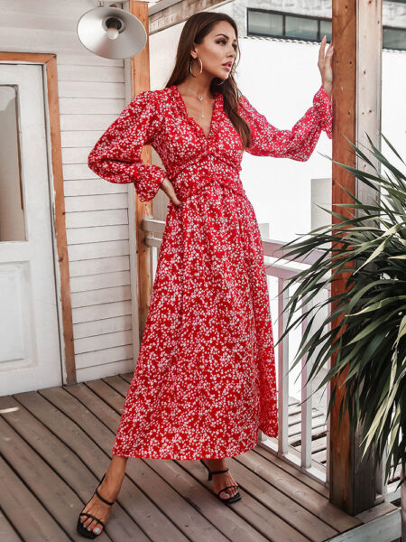 Femme portant une robe longue rouge à fleurs blanches avec des sandales noires aux pieds. Elle se trouve sur un balcon en bois