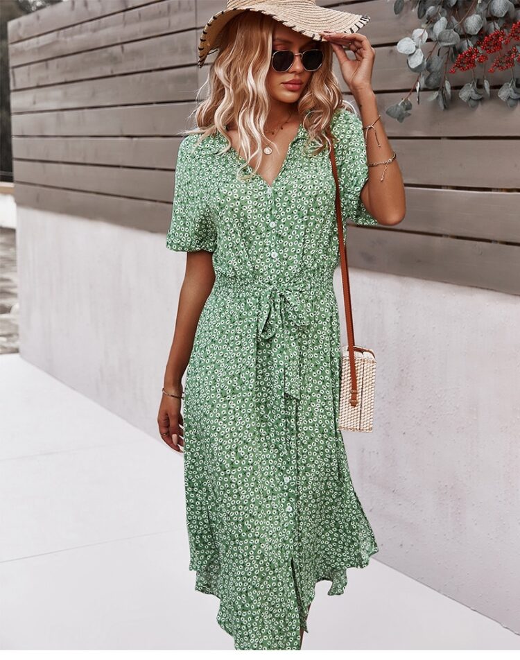 Femme portant une robe fleurie verte mi-longue avec un sac en paille sur son épaule gauche ainsi qu'un chapeau sur la tête et des lunettes de soleil