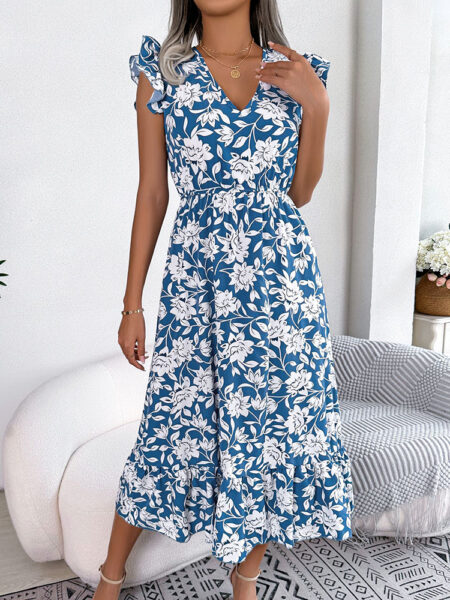 Longue robe imprimée à col en V pour femme bleue, portée par une femme debout devant un canapé blanc