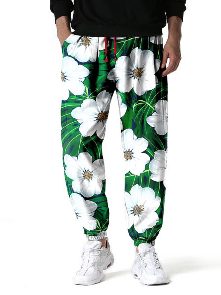 Pantalon de couleur vert avec des motifs de fleurs blanches, porté par un homme avec des baskets blanches et un haut noir
