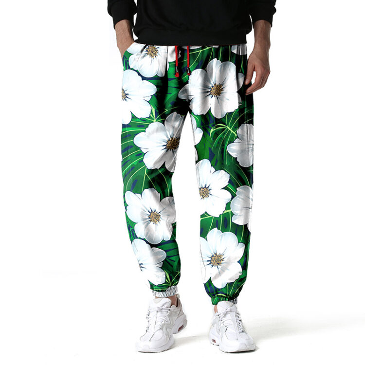 Pantalon de couleur vert avec des motifs de fleurs blanches, porté par un homme avec des baskets blanches et un haut noir
