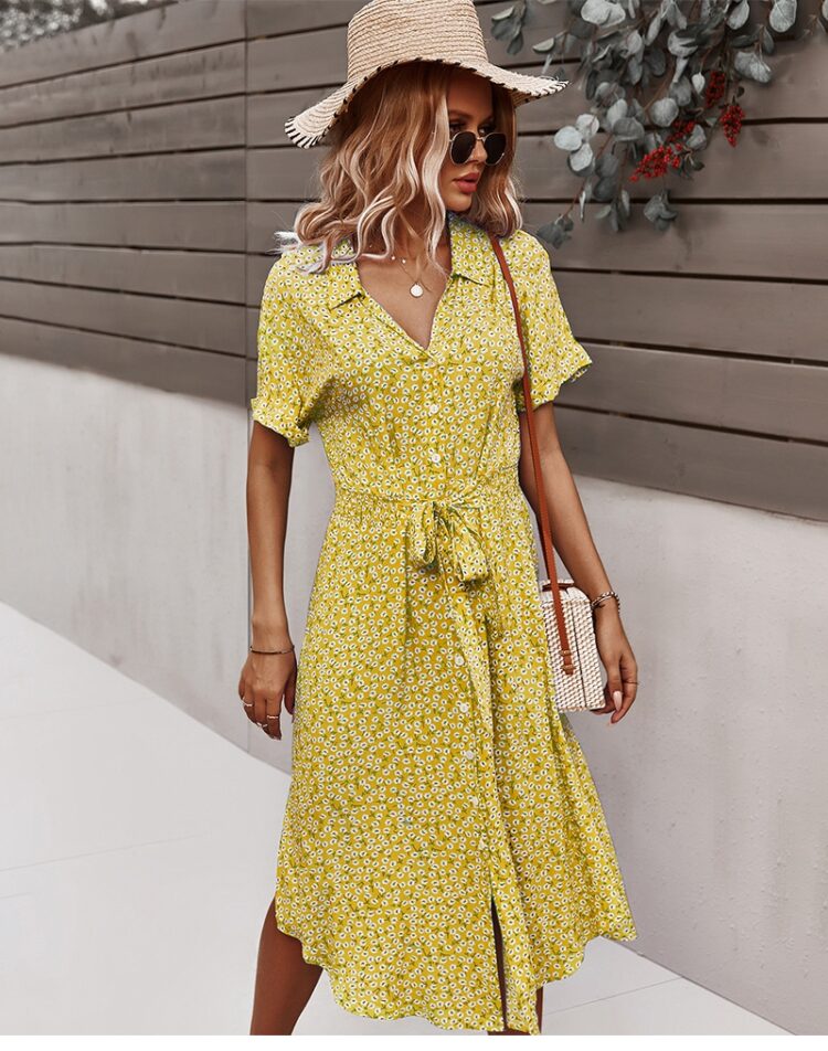 Femme portant une robe fleurie jaune mi-longue avec un sac en paille sur son épaule gauche ainsi qu'un chapeau sur la tête et des lunettes de soleil