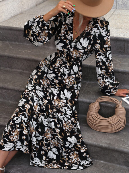 Robe longue à imprimé floral et col en V à manches longues de couleur noire, portée par une femme assise sur des escaliers avec à ses côtés un sac à main beige et portant un chapeau beige